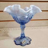 Front and side photo showing the entire blue glass bowl with ruffled edge, textured stem, and scalloped base with label.