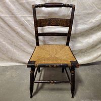 Full frontal image of the Hitchcock style chair showing the woven rattan seat and dark wooden frame with decorative painted accents.