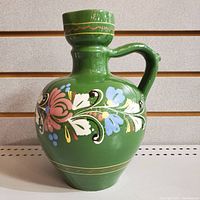 Front and side view of green hand painted jug with floral designs and handle, showing overall shape and colors.