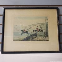 Framed print of hunting scene with two riders jumping a fence, dogs and landscape background.
