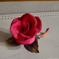 Porcelain red rose flower figurine with visible broken stem piece placed next to it