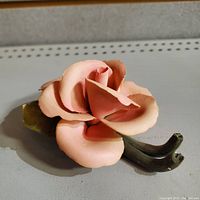 Top angle view of pink porcelain rose bloom with visible petal details and a green stem with leaf on a flat surface.
