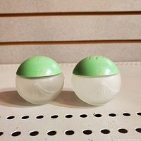 Front angle photo of two satin glass spherical salt and pepper shakers with embossed art deco tassel design and jadeite green curved plastic caps.
