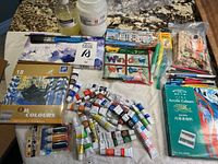 Overview of artist supplies including multiple tubes of paints, window writers, brushes, pencil crayons, popsicle sticks and bottles of liquids