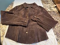 Brown suede jacket laid flat on surface showing front, collar, sleeves and snap button details.