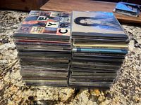 Two stacks of music CDs on a granite countertop, showing a substantial lot of mixed genre albums and recordable discs.