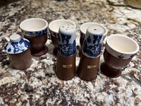 Top and front view of the set showing four egg cups and two shakers with blue floral motifs and brown bases on a granite countertop