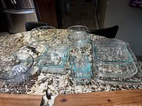 Entire collection of 16 Pyrex glass bakeware pieces arranged on granite countertop, showing various nested rectangular, square, round bowls and pie plates.