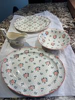 Set of Johnson Brothers Monticello serving dishes including two oblong platters, gravy boat, and fruit bowl arranged on cloth.