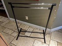Metal coat rack with black frame, showing full front view at base dimensions on tile floor.