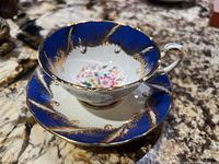 Overall view of the teacup and saucer on a marble surface showing the blue and gold design with multi-colored floral interior.