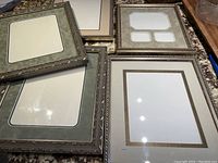 Box of various professionally matted picture frames with decorative metal-toned borders and different mat colors and window configurations.