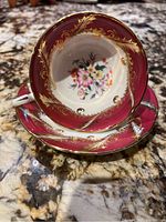Top view showing red border, gold detailing, and multi-colored floral pattern inside the teacup and on the saucer.