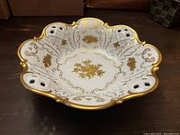 Top view of white scalloped porcelain bowl with pierced lattice design and intricate 22K gold floral and leaf patterns inside.