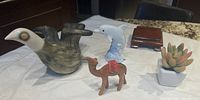 Overview of all five items: ceramic bird, ceramic dolphin on base, wooden camel, small faux succulent, wooden stand.
