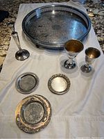 Top view of silver plated tray, goblets, candle holder, and small dishes on white cloth on a granite counter