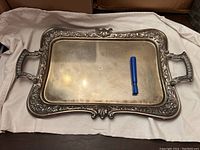 Full view of rectangular silver plate tray with ornate handles and floral-scrollwork border. Blue marker pen placed on tray for scale.