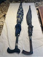 Two umbrellas closed and laid flat on a white cloth, showing the canopy patterns and walking stick handles.