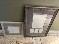 Two professional picture frames: a smaller white ornate frame with beige matting and a larger ornate frame with dark matting and multiple picture openings.