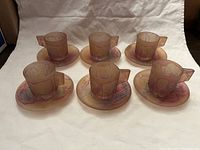 Full set of 6 pink Rueven art glass demitasse cups and matching saucers displayed on white cloth background.