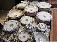 Full view of the Wedgewood Hampton china set on countertop, includes stacked plates, bowls, platters, sugar bowls, creamer, and fruit bowls with lids.