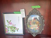 Two framed floral paintings displayed side by side: the Edward Bary oil painting in an ornate metal oval frame and the Howard Johnston floral painting in a simple rectangular plastic frame.