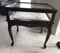 Front view of the rectangular display table with glass top and drawer below, showing curved legs.