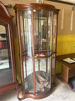 Front view of a curved cherry wood display cabinet with glass and plexiglass panels, showcasing its shape, material, and interior space.