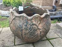 Heavy ceramic planter outdoors on a stone patio showing leaf textured design and scalloped rim.