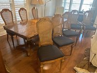 Full view of 8 wood chairs with cane backs and upholstered seats, including 2 armchairs and 6 side chairs around a wooden table.