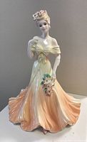 Front view of Coalport porcelain figurine displaying detailed face, floral hairpiece, and flowing peach-orange gown.