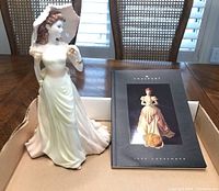 Photo showing the Coalport 'Vicky' figurine alongside the 1996 Coalport catalog inside a box.