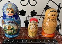 Photo showing three nesting dolls placed side by side on a woven surface with a measuring ruler below for size reference.
