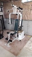Full view of the exercise machine with padded seat, leg rollers, and metal frame on carpet in basement.