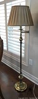 Full floor lamp with beige pleated shade and brass style base shown near window
