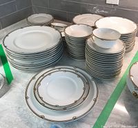 Stacked dinner, salad, and bread plates with ornate gold and black border patterns on white porcelain.