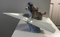 Side angled view of Lladro puppy figure on paper airplane with cloud base.