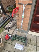 Side view of Lee Valley 15 cut manual push mower and Homelite electric trimmer together leaning against the brick wall.