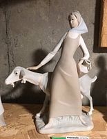 Front and side view of NAO Lladro porcelain figure of a woman standing with a goat, showing the woman holding a ceramic pitcher.