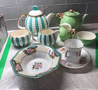 H.J Wood striped tea set in turquoise with gold accents including teapot, creamer, and sugar bowl; Royal Winton green tea set with pink flower details; Hammersley floral teacup and saucer; Noritake octagonal bowl with floral pattern.