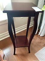 Front view of the dark stained wooden plant stand with curved legs and lower shelf, showing overall structure and condition.