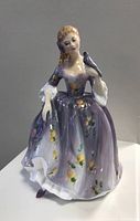 Front view of Royal Doulton Nicola figurine in lavender floral dress holding a bird.