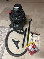 Whole Shop Vac unit with hose, extension wands, nozzle, and unopened replacement filter bags visible on concrete floor.
