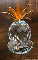 Front view of Swarovski crystal pineapple with gold-toned metal leaves on a glass mirror base