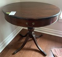 Full view of the dark stained wood round table showing single pedestal base with curved legs and brass feet, table top visible with no major damage.
