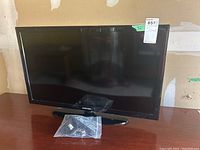 Front view of Samsung 32-inch TV with remote and cables laid in front in plastic bag.