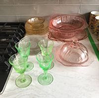 Set showing green etched glasses, pink bowls, amber plates, and clear etched plates on countertop.