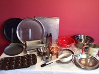 Wide shot showing variety of pans, bowls, measuring cups, grater, juicers, and rolling pin all arranged together on a table.