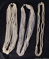 Three multi-strand pearl necklaces in off-white shades, displayed on black background.