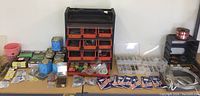 Wide photo showing entire hardware lot with storage organizers, packages, and loose items spread on a table.
